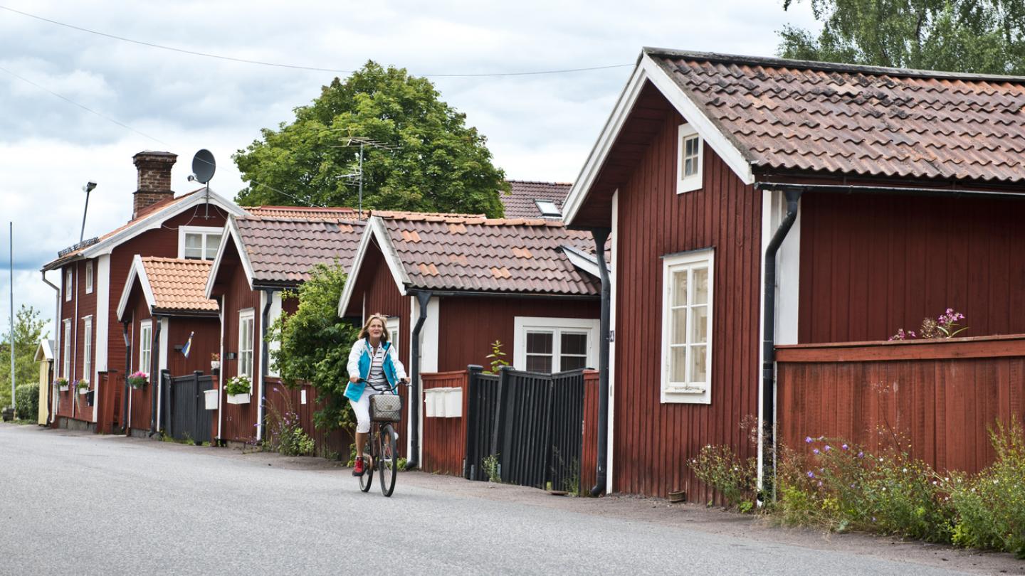 Kvinna cyklar i trästaden Elsborg bland Faluröda hus.