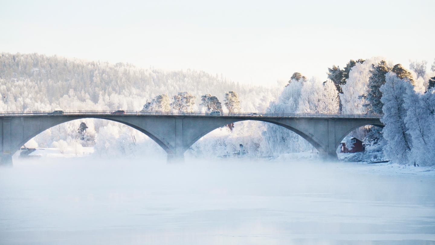 Bilar kör över en bro över vintrig älv.