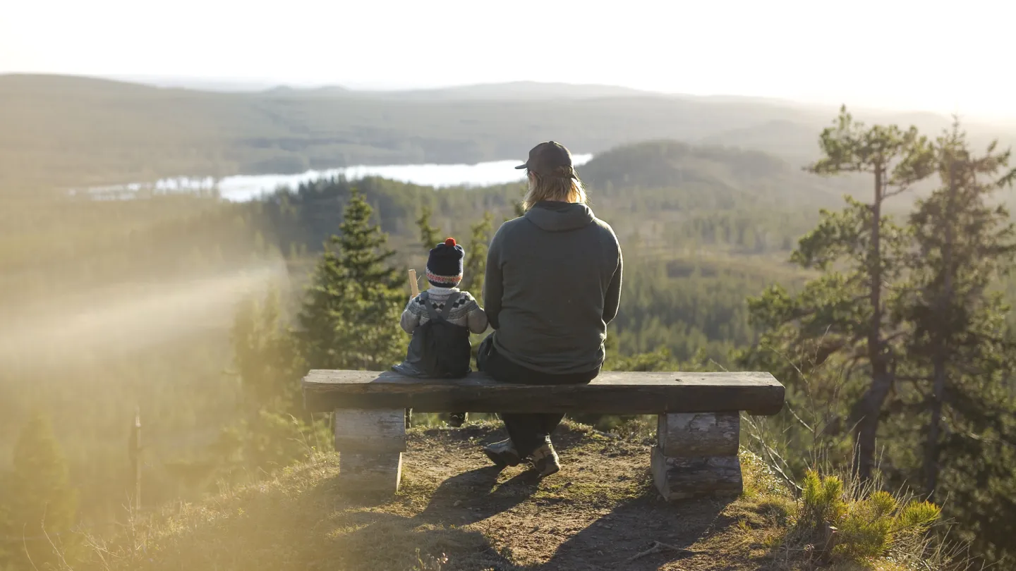 En vuxen med ett barn på en parkbänk som kollar ut över höstliga ustikten.
