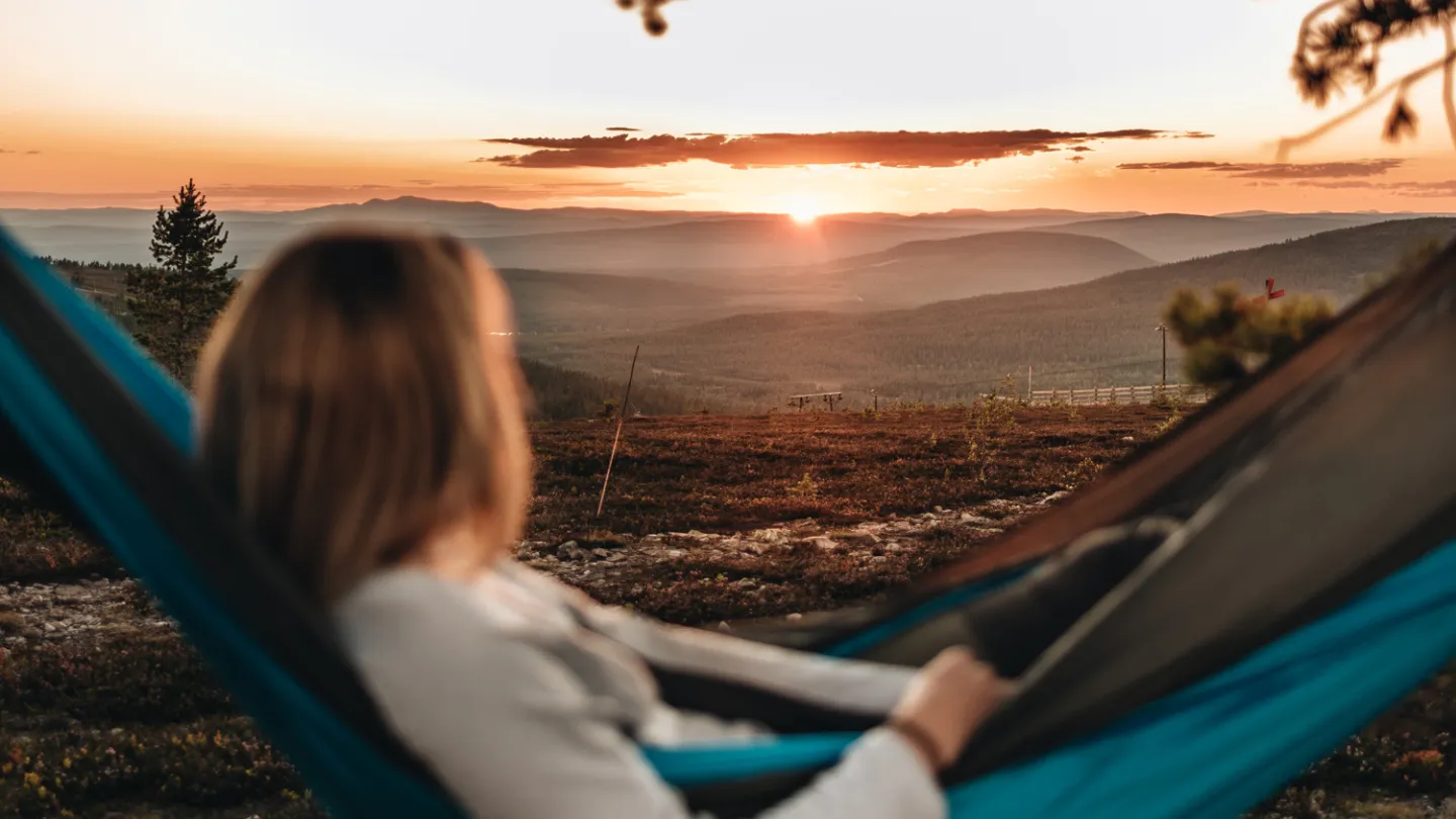 A woman in a hammock looking at the sun set.