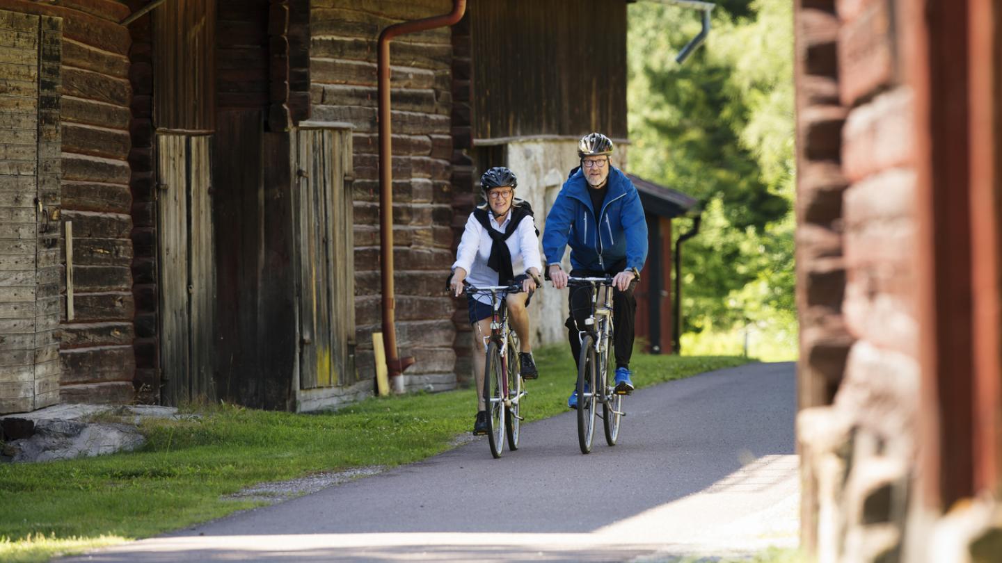 Par som cyklar på väg mellan fina röda trähus.