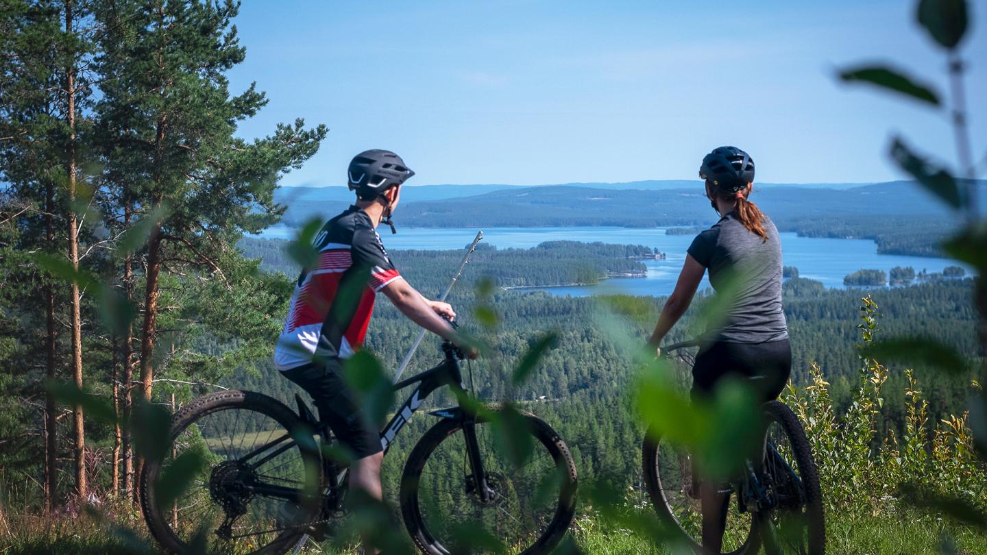 Ett par på cykel kikar ut från en höjd mot en sjö.