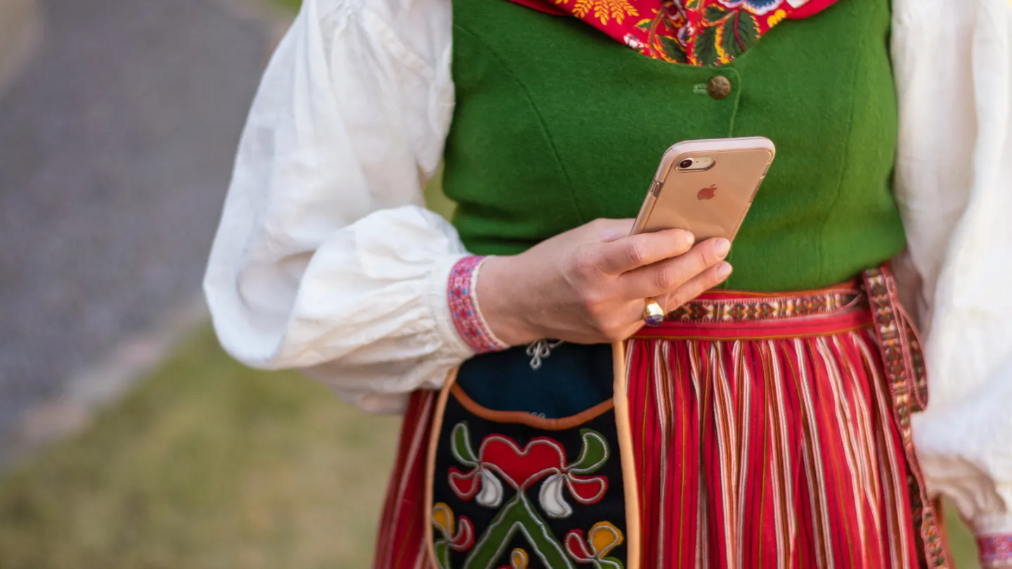 Kvinna i folkdräkt håller i mobiltelefon.