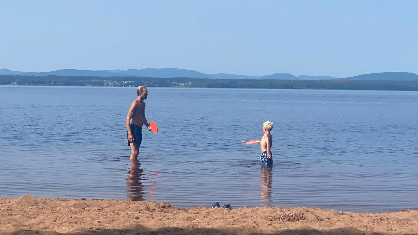En man och en liten pojke spelar strandtennis i vattenbrynet i en sjö.