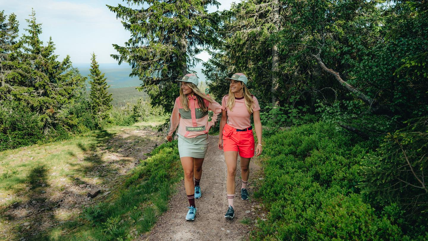 Två kvinnor går på en vandringsled i skogen.