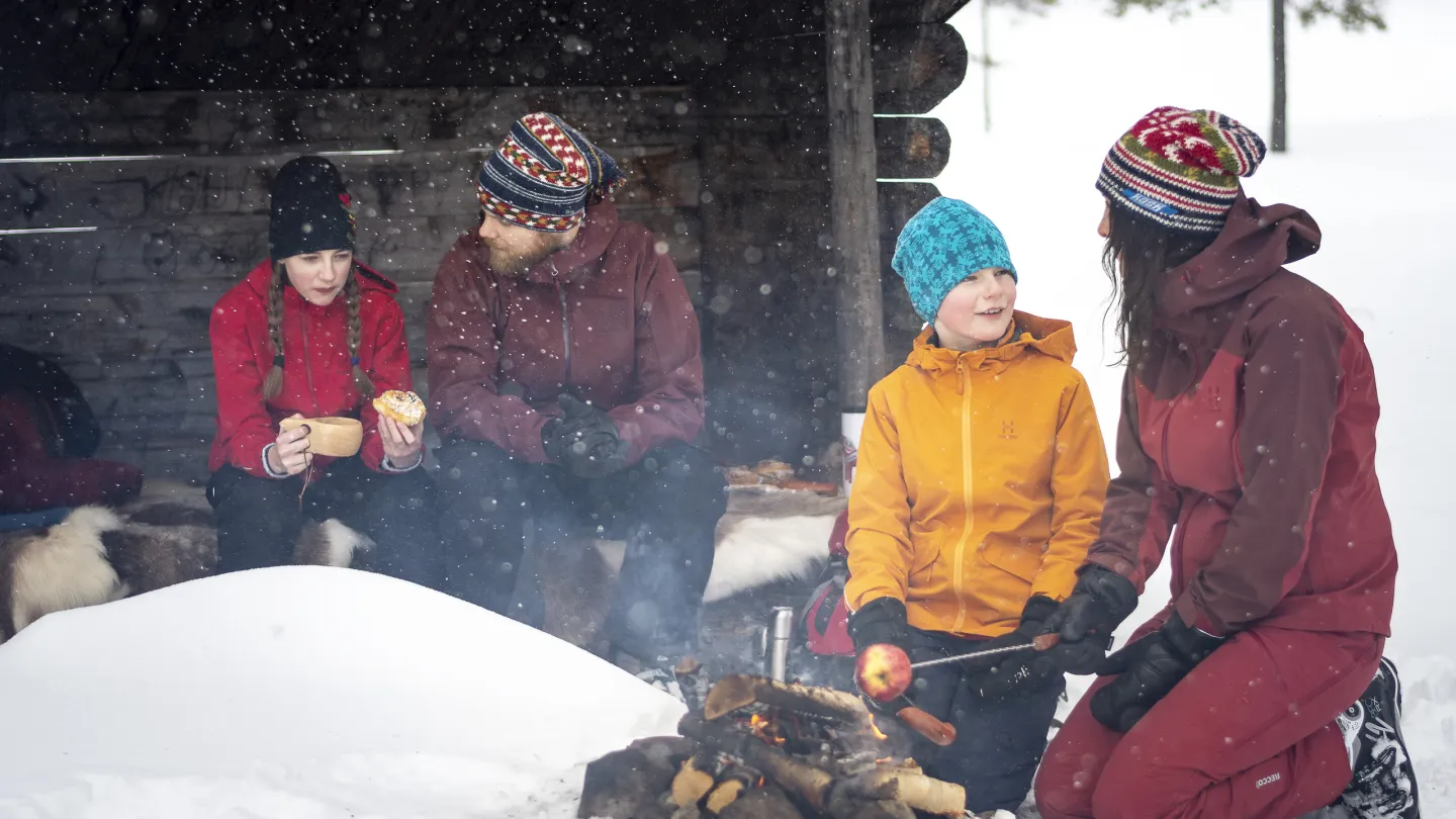 Familj som myser i snön vid en slogbod