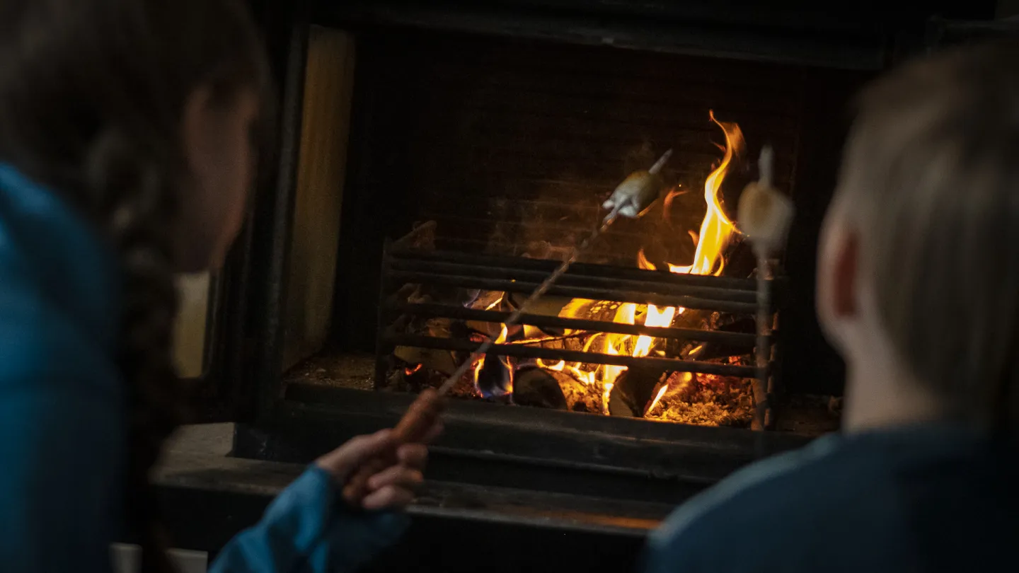 Två barn som grillar marshmallows i öppen spis.