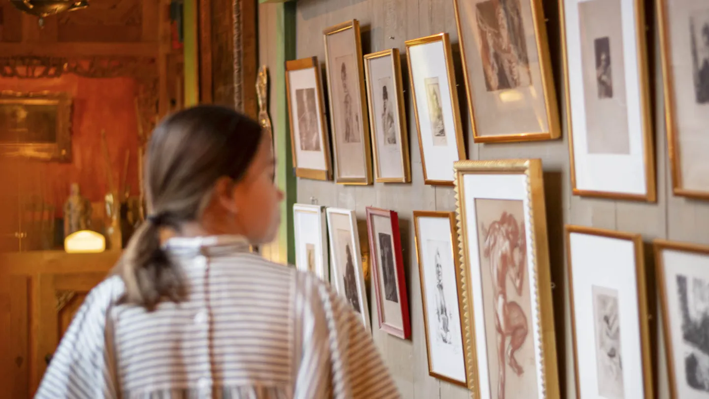 A guide at Carl Larsson-gården walking pass a wall full of paintings.