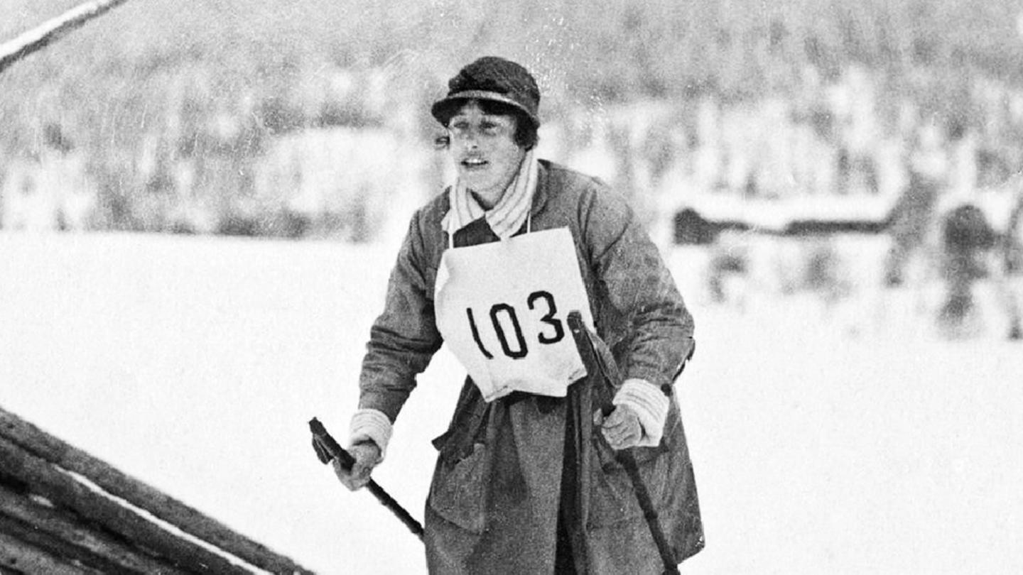 Svartvit äldre bild på en kvinna som åker skidor med nummerlappen 103 på bröstet.
