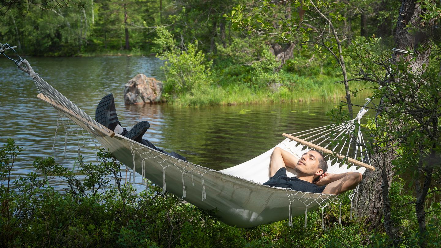 En man vilar i en hängmatta vid ett vattendrag.