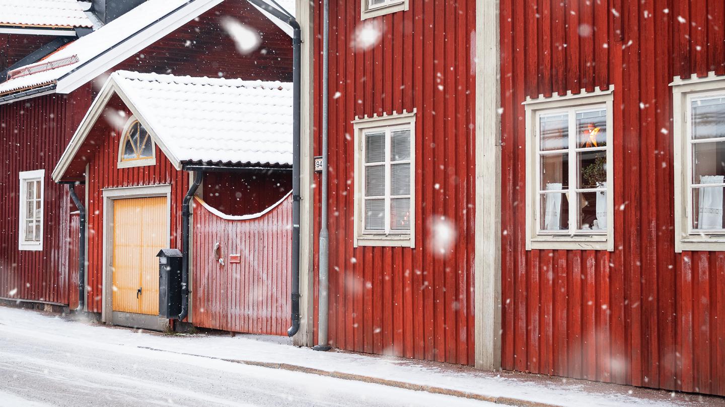 Det snöar längs en gata med röda trähus i Falun, Östanfors.